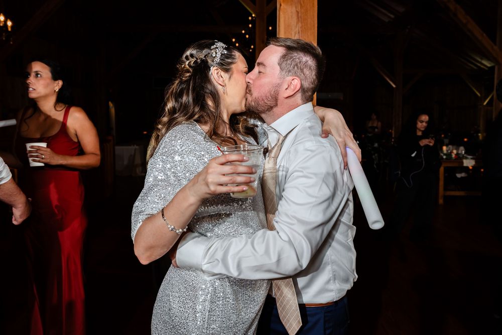 Bride and groom kissing while holding drinks on the wedding reception dance floor.