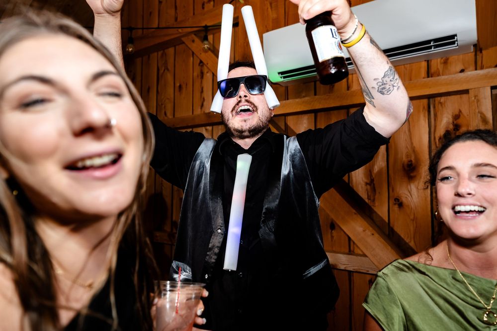 Guest in novelty glasses raises bottle at energetic barn wedding party.