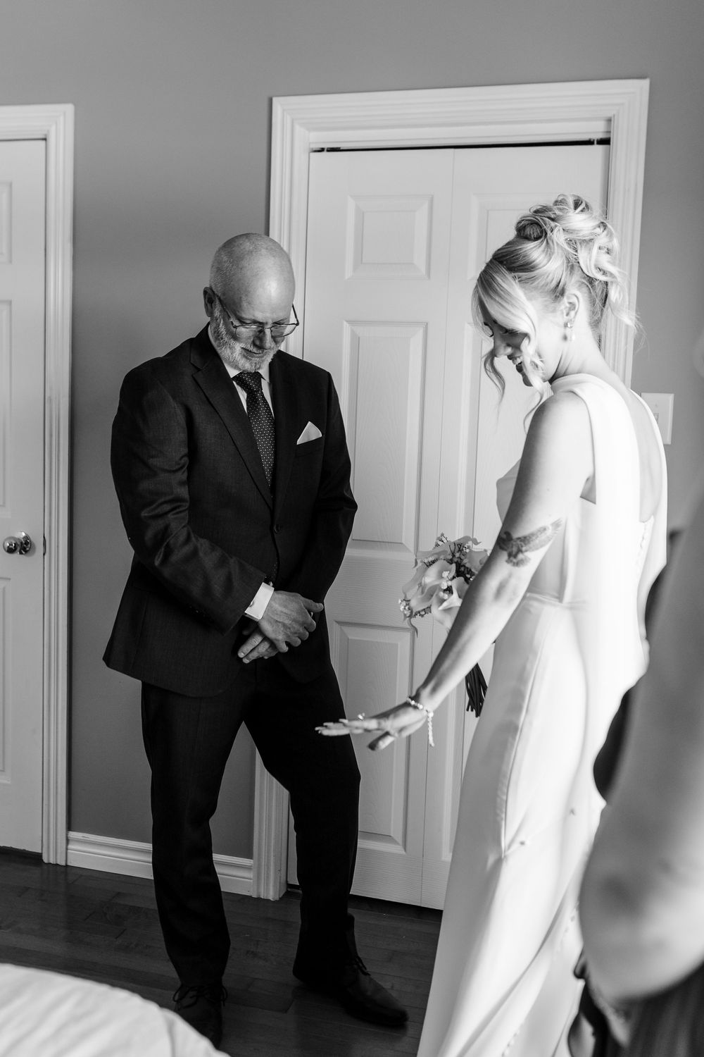 Black and white photo of a bride in a white gown sharing a tender moment with an older man in a suit before her wedding.