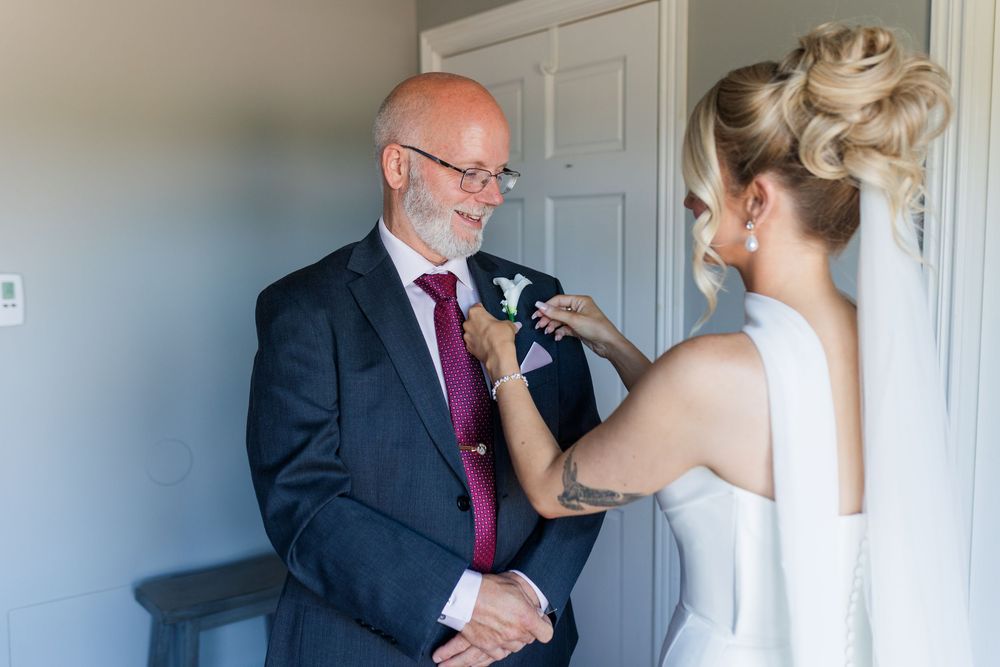 Bride pinning a boutonniere on her father's suit lapel before the wedding ceremony.