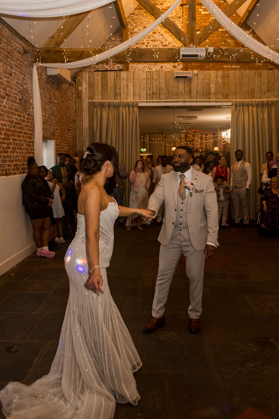 Bride and groom share their first dance in a rustic barn venue with exposed brick walls and fairy lights.