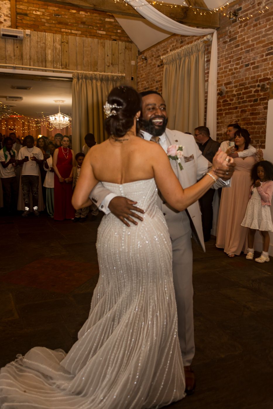 A bride and groom share their first dance at a wedding reception in a rustic brick venue.