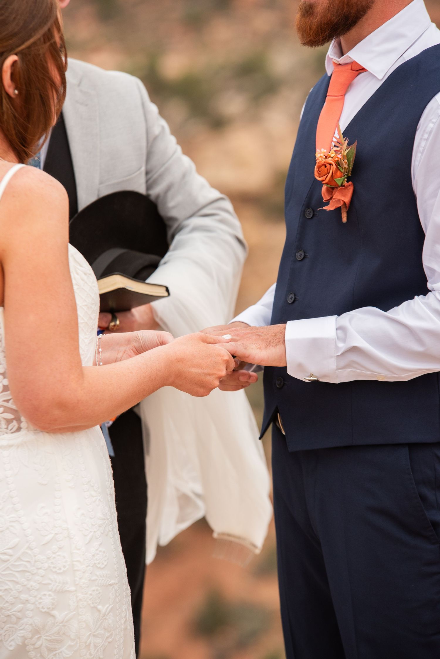 Bride and groom celebrate on rocky overlook with red rock canyon views, bride raising bouquet in white gown, groom in navy suit.