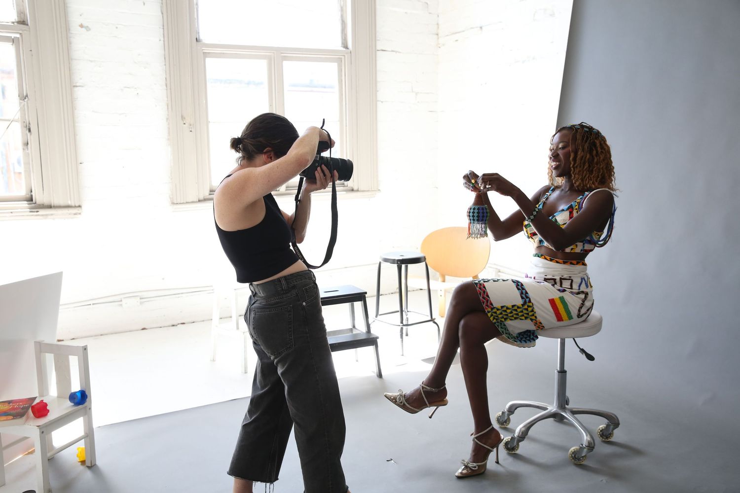 Photographer taking pictures of a model sitting on a chair in a bright studio setting.