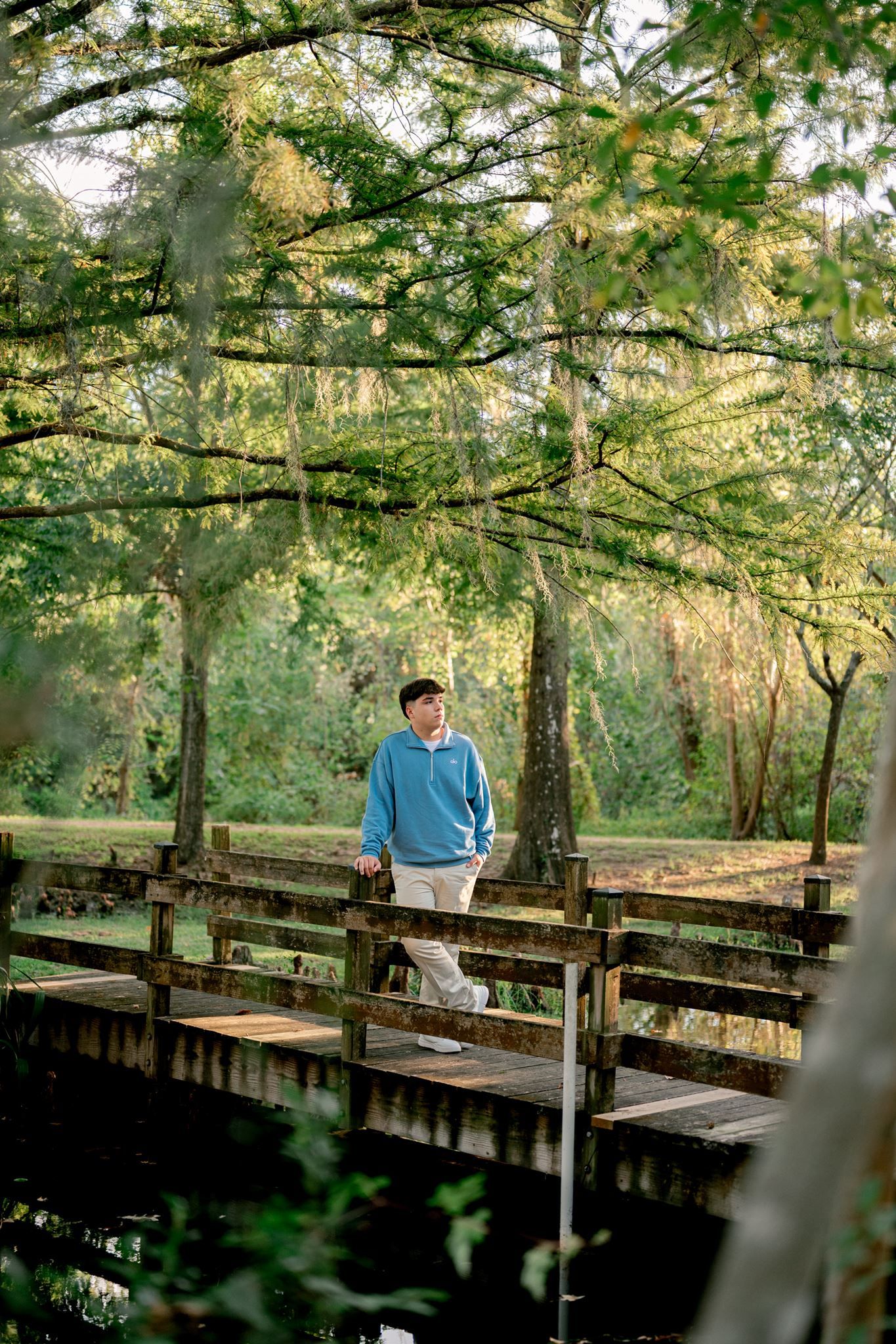 Senior guy standing on bridge under a mossy tree.