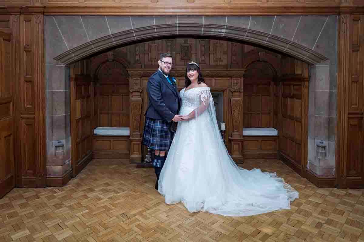 Bride and groom stand in front of the master fire place in Dalston Hall