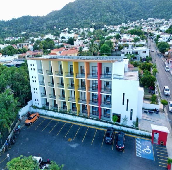 Aerial view of modern five-story white commercial building with colorful accents and parking lot.