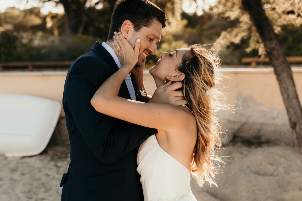 A romantic couple embraces and laughs together on a beach at sunset.