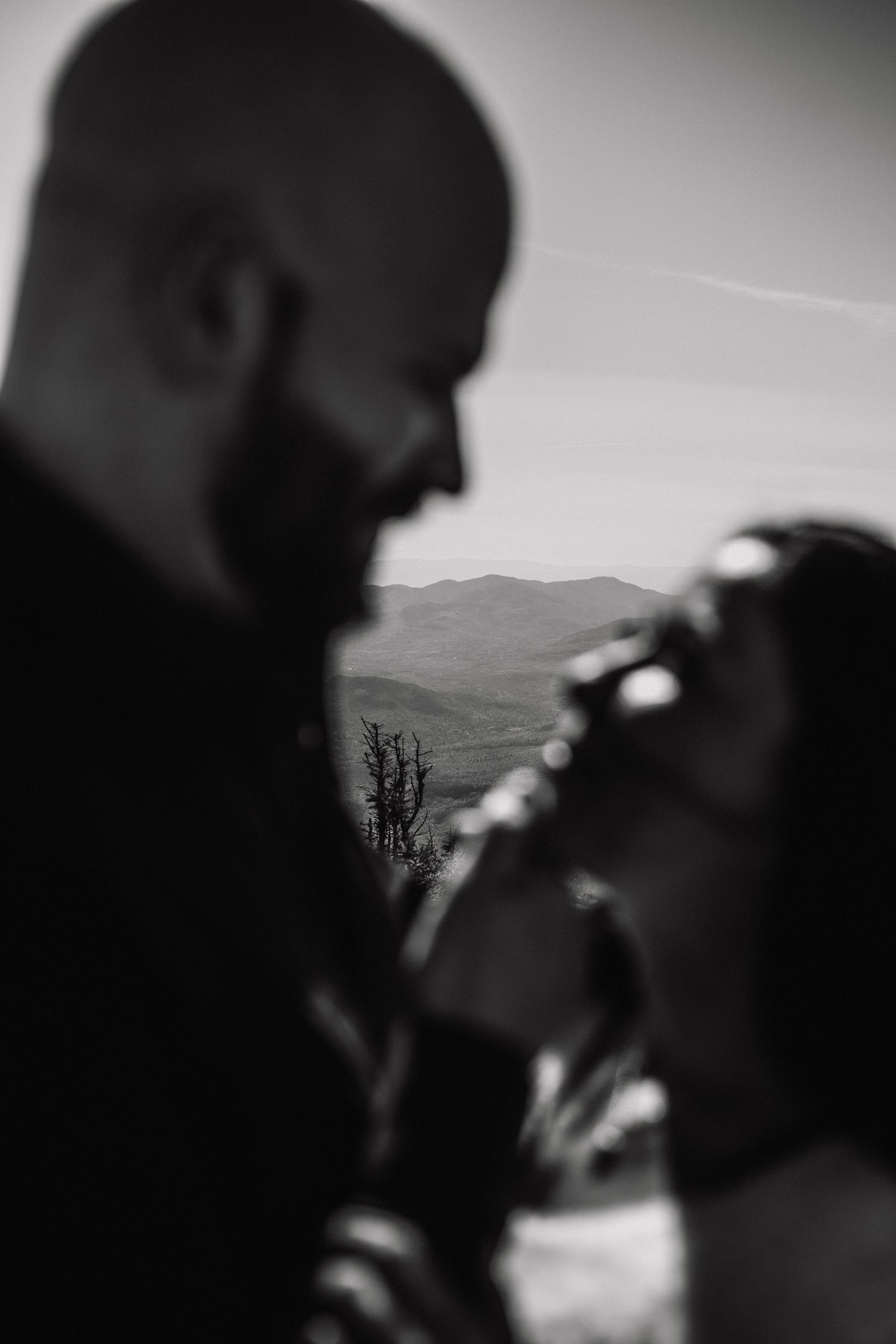 Romantic black and white silhouette of couple about to kiss with mountain landscape softly blurred in background.