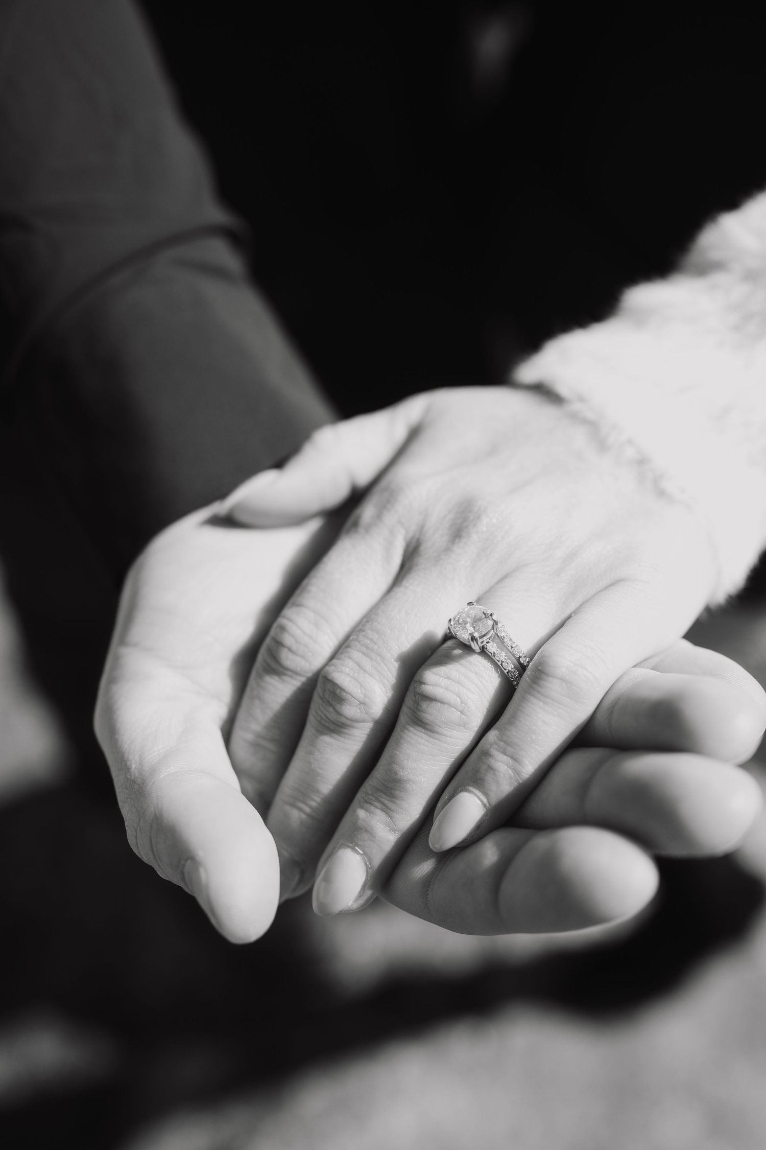Black and white close-up of two hands touching, one wearing a diamond engagement ring.