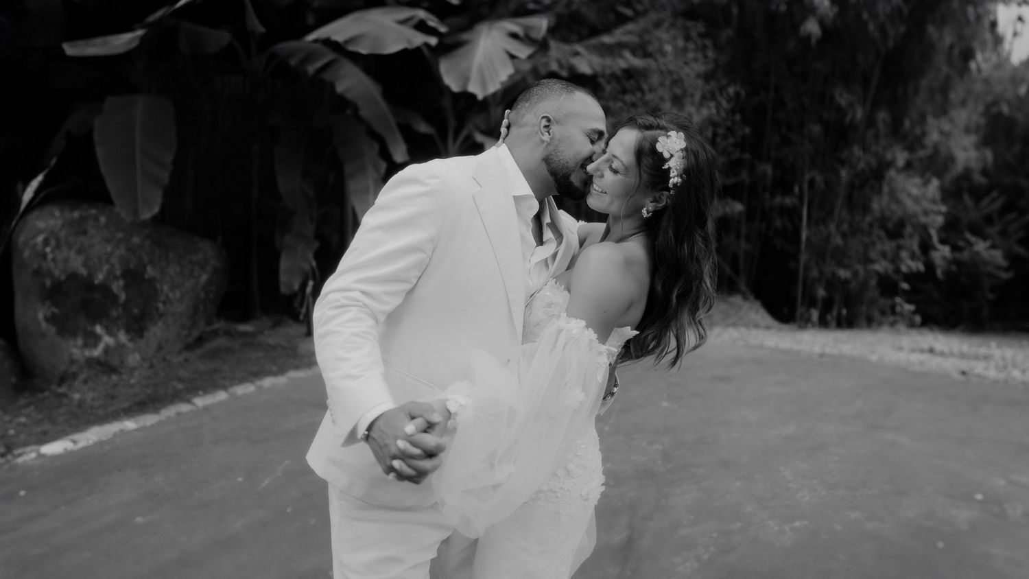 A couple dressed in white attire share a romantic dance dip pose together in a black and white photograph.