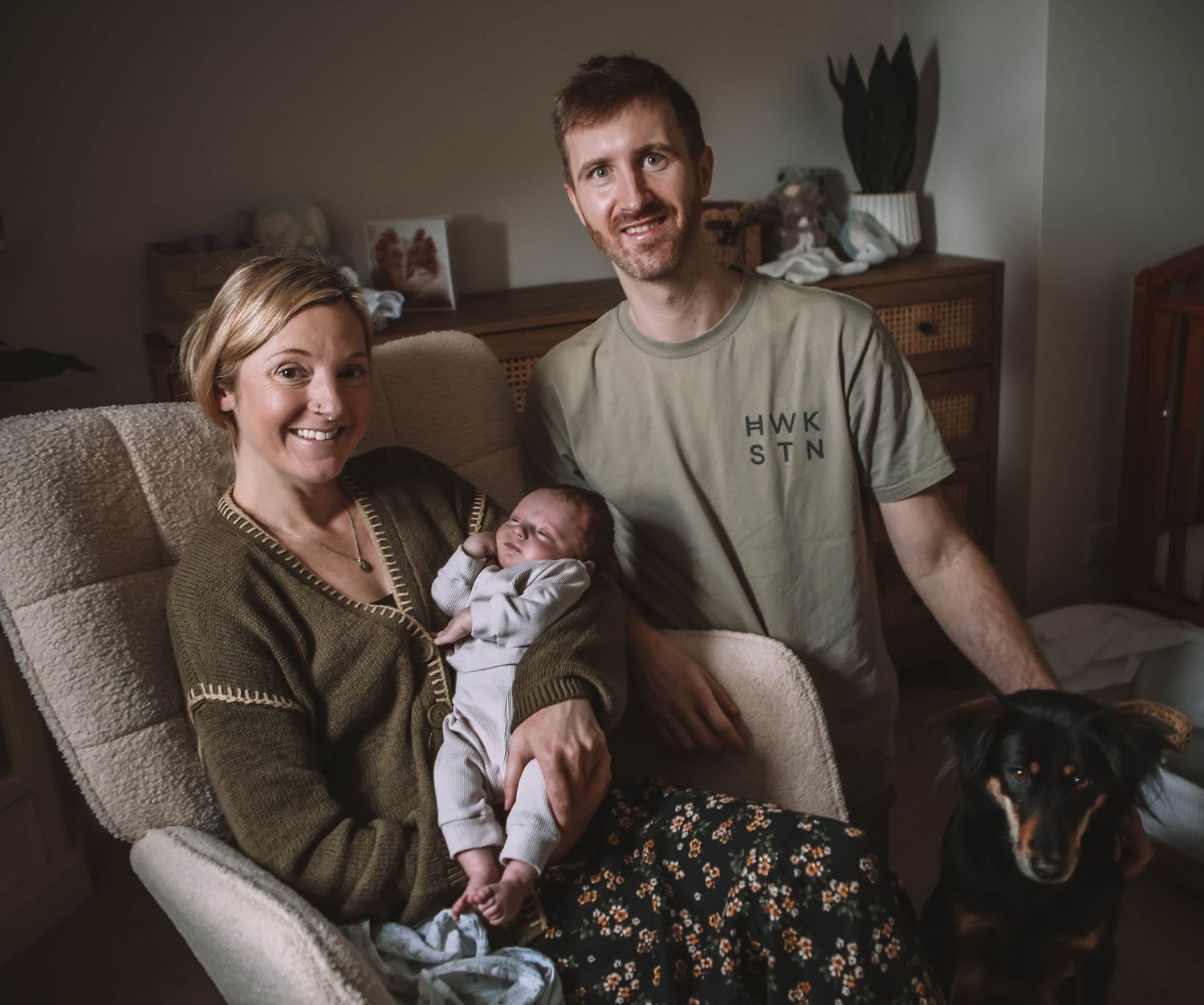 Parents lovingly holding their newborn baby wrapped in white swaddle while older sibling watches nearby.