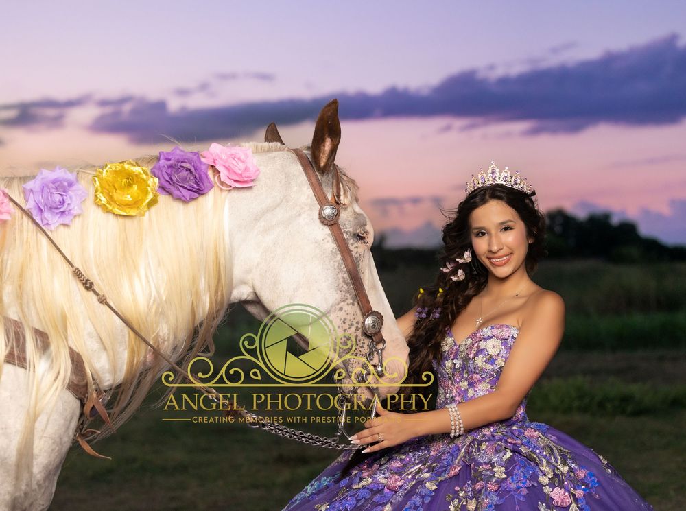 Young woman in purple quinceañera gown poses with white horse adorned with flowers at sunset.