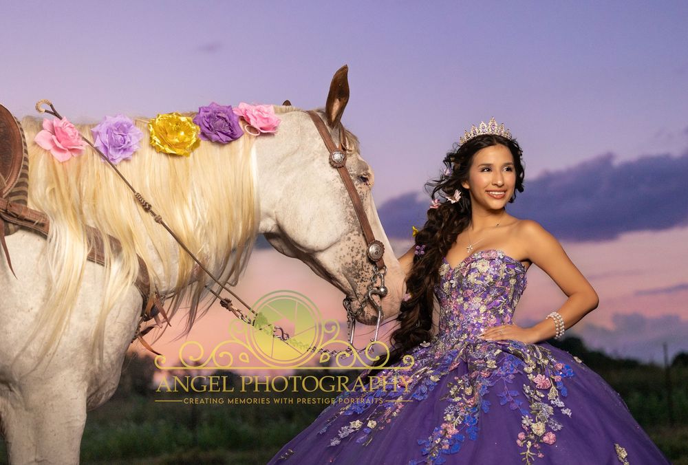 Young woman in purple quinceañera gown with tiara poses beside a decorated white horse at sunset.
