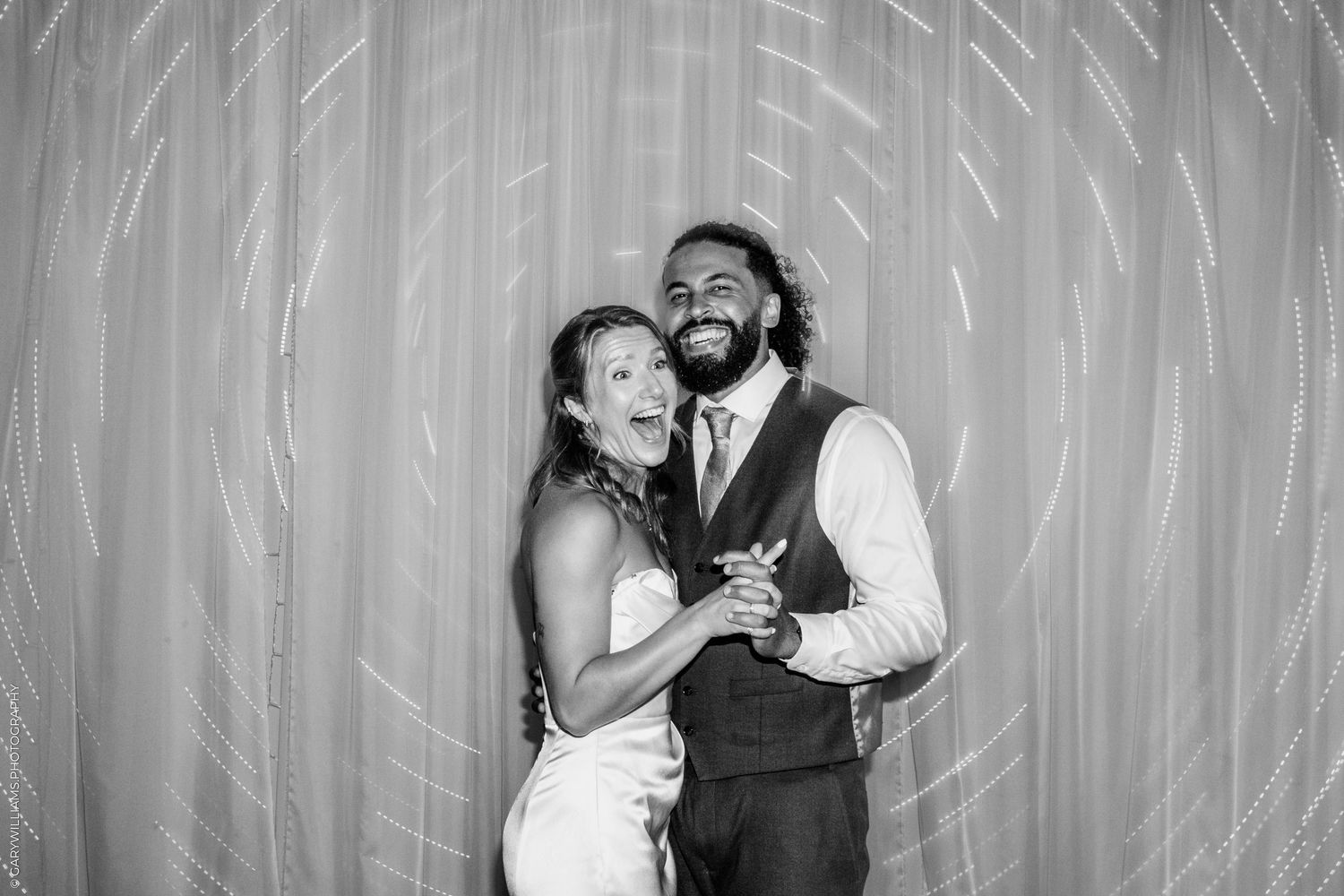 Black and white photo of a smiling bride and groom posing together in a photo booth at their wedding reception.