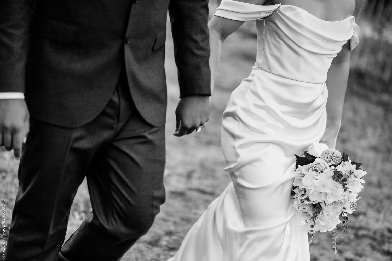 Black and white photo of a bride and groom holding hands, bride in elegant white gown holding a bouquet.