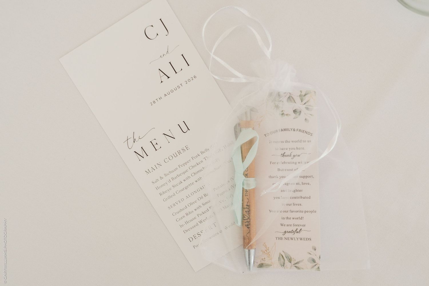 Elegant wedding menu cards with floral accents, a kraft paper scroll tied with blue ribbon, on white background.