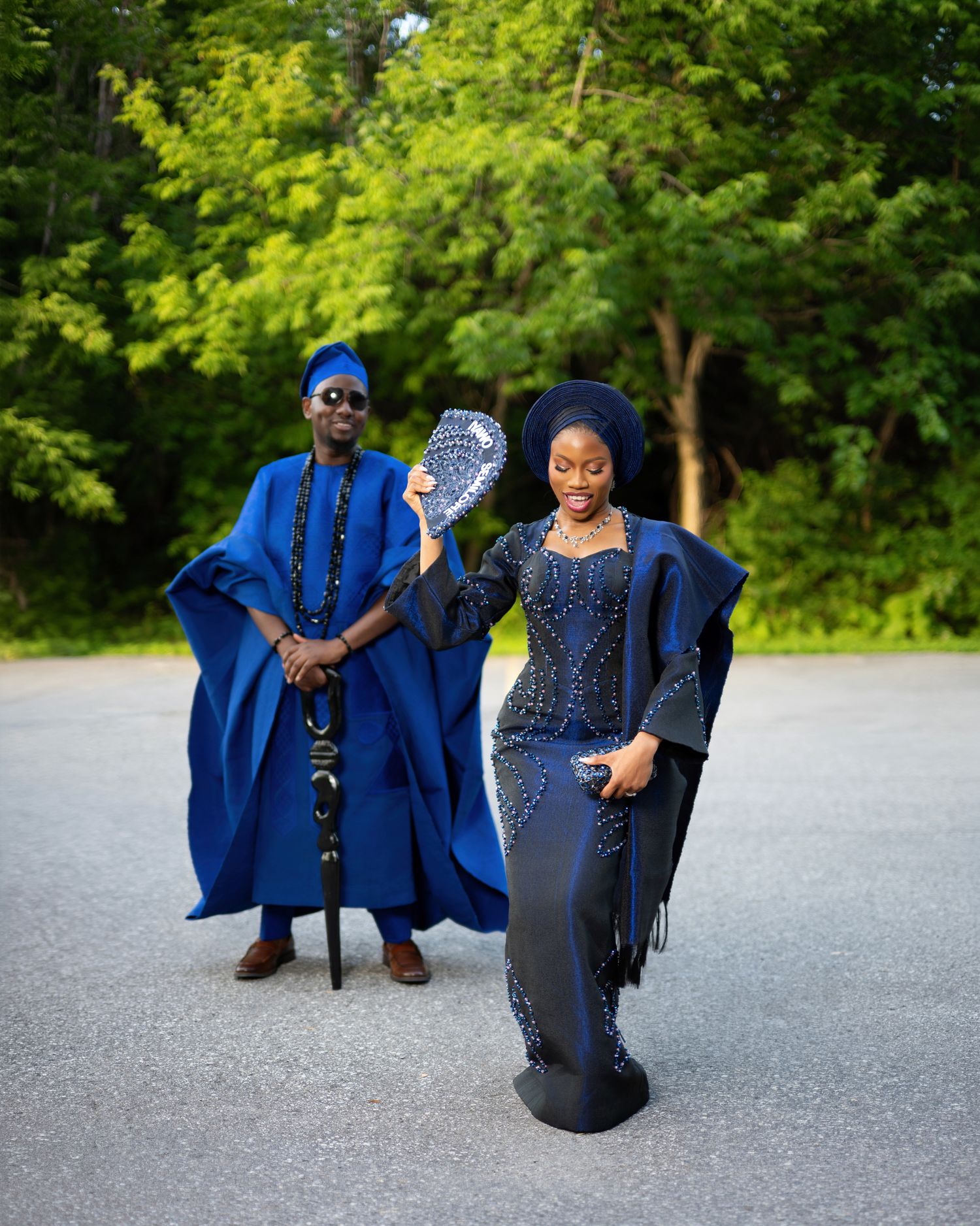 Couple in elegant Nigerian traditional attire, man in royal blue agbada with cap, woman in beaded navy gele and gown.
