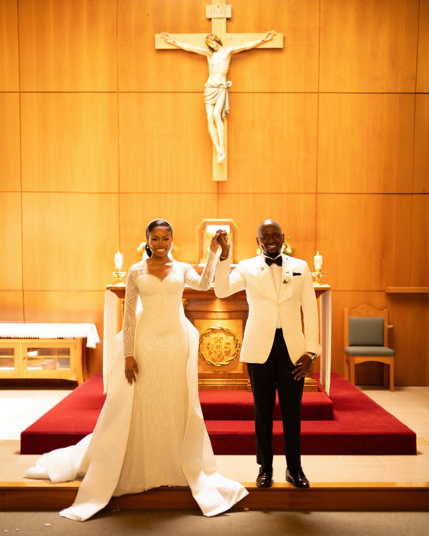 Bride and groom celebrate at church altar beneath crucifix in classic white wedding attire.
