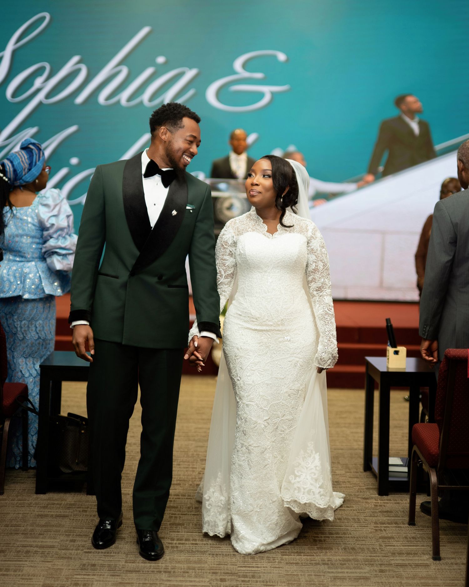 Bride and groom share a joyful glance during their wedding ceremony, groom in green tuxedo, bride in lace gown.