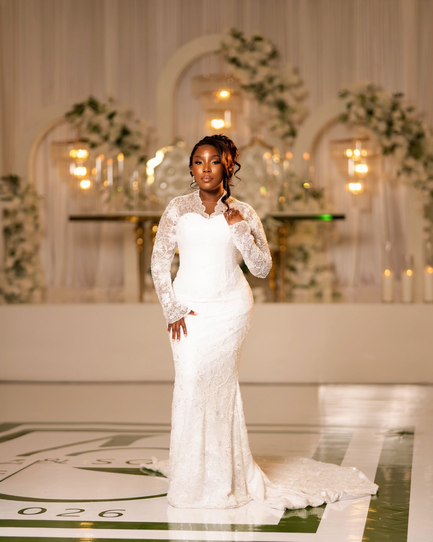 Elegant bride in a long-sleeve lace mermaid wedding gown posing in a beautifully decorated wedding venue.
