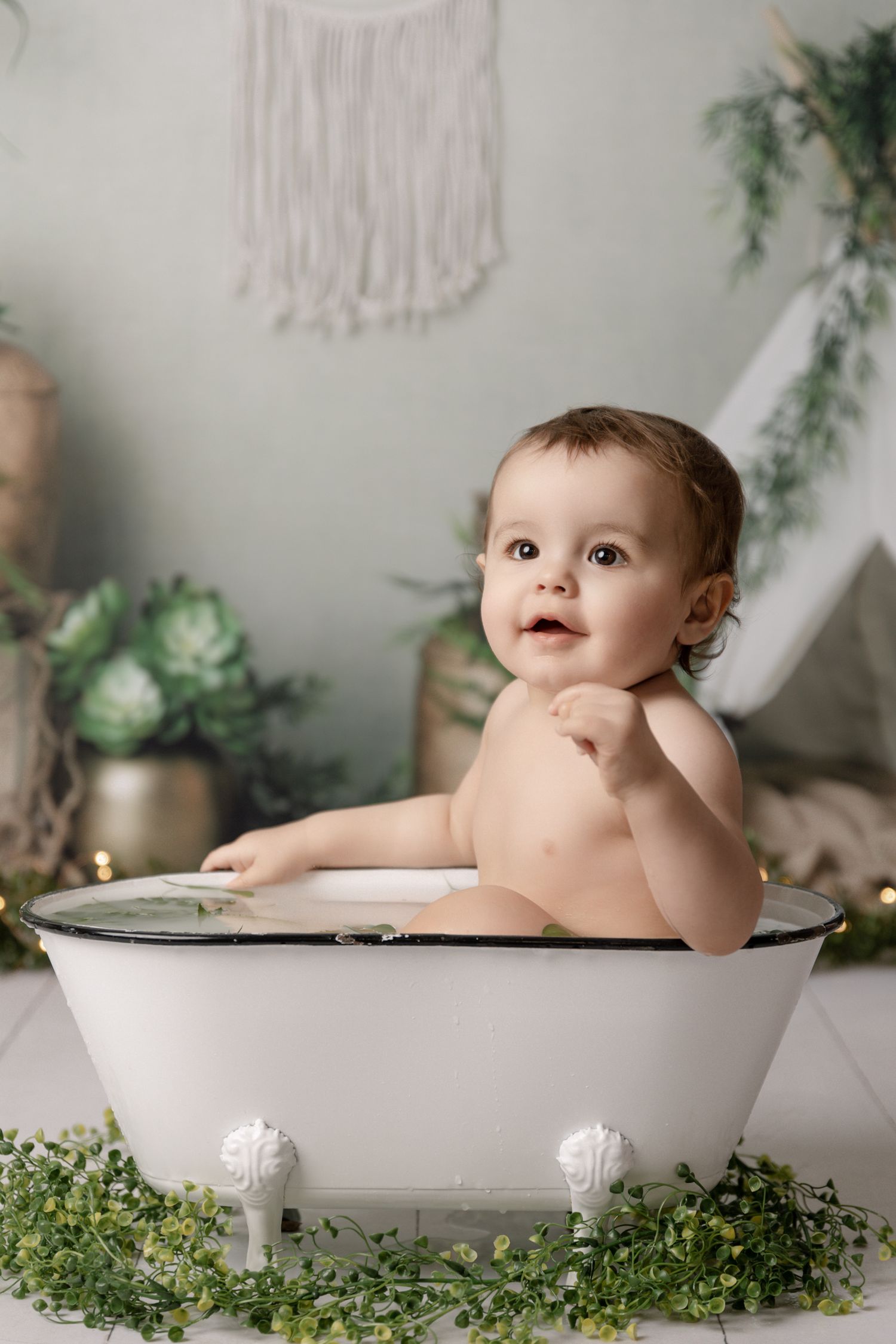 Baby sitting in a white vintage tub in a neutral greenery-filled studio set