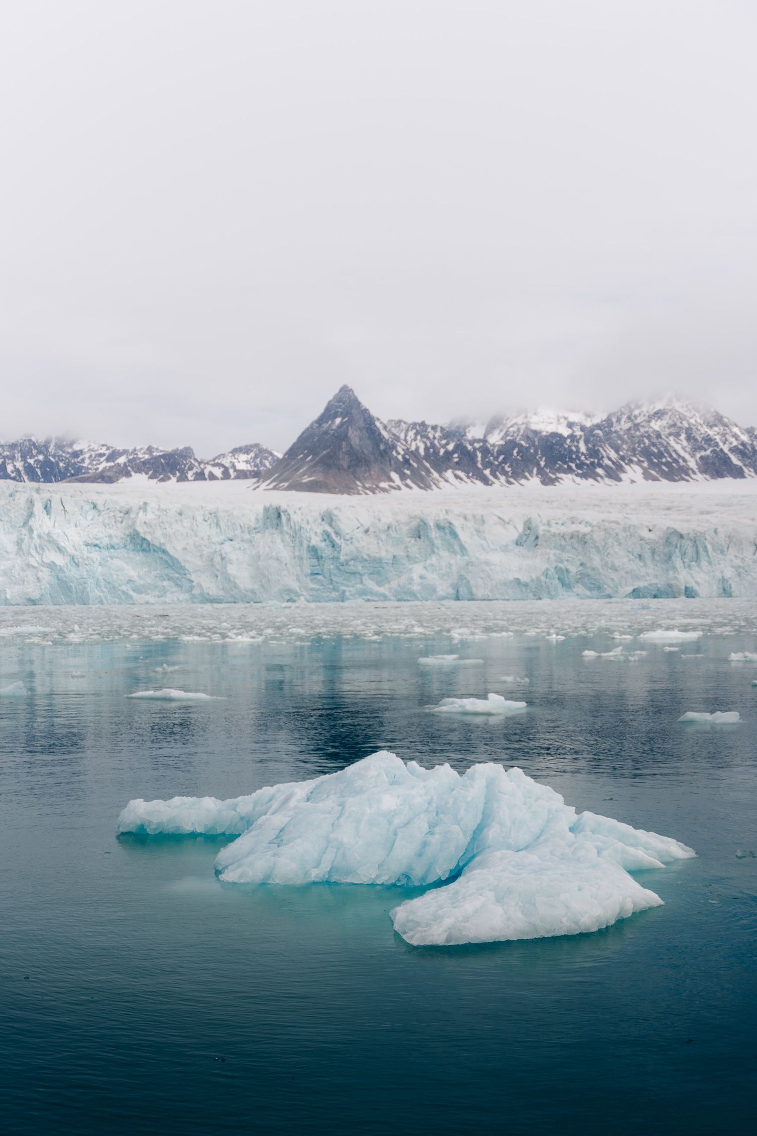 Iceberg bleuté devant un sommet sombre et un front glaciaire du Svalbard