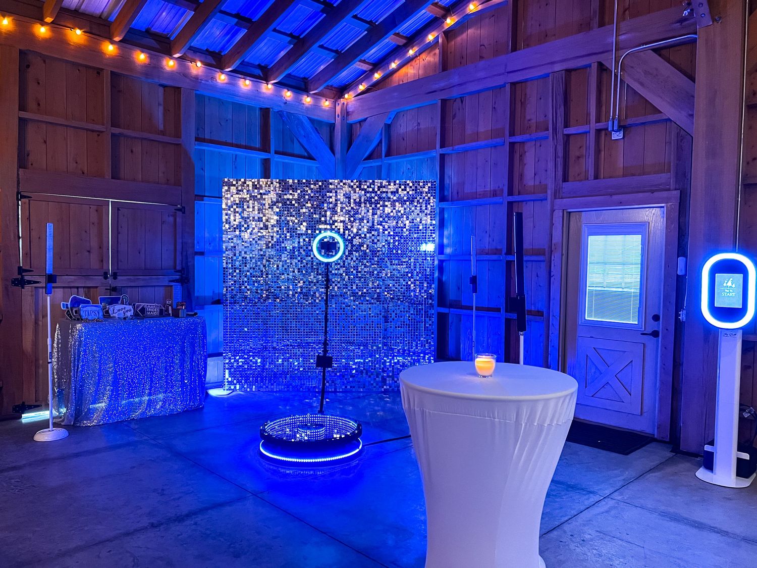 Elegant photo booth setup with sequin backdrop, ring light, and blue ambient lighting inside a rustic barn venue.