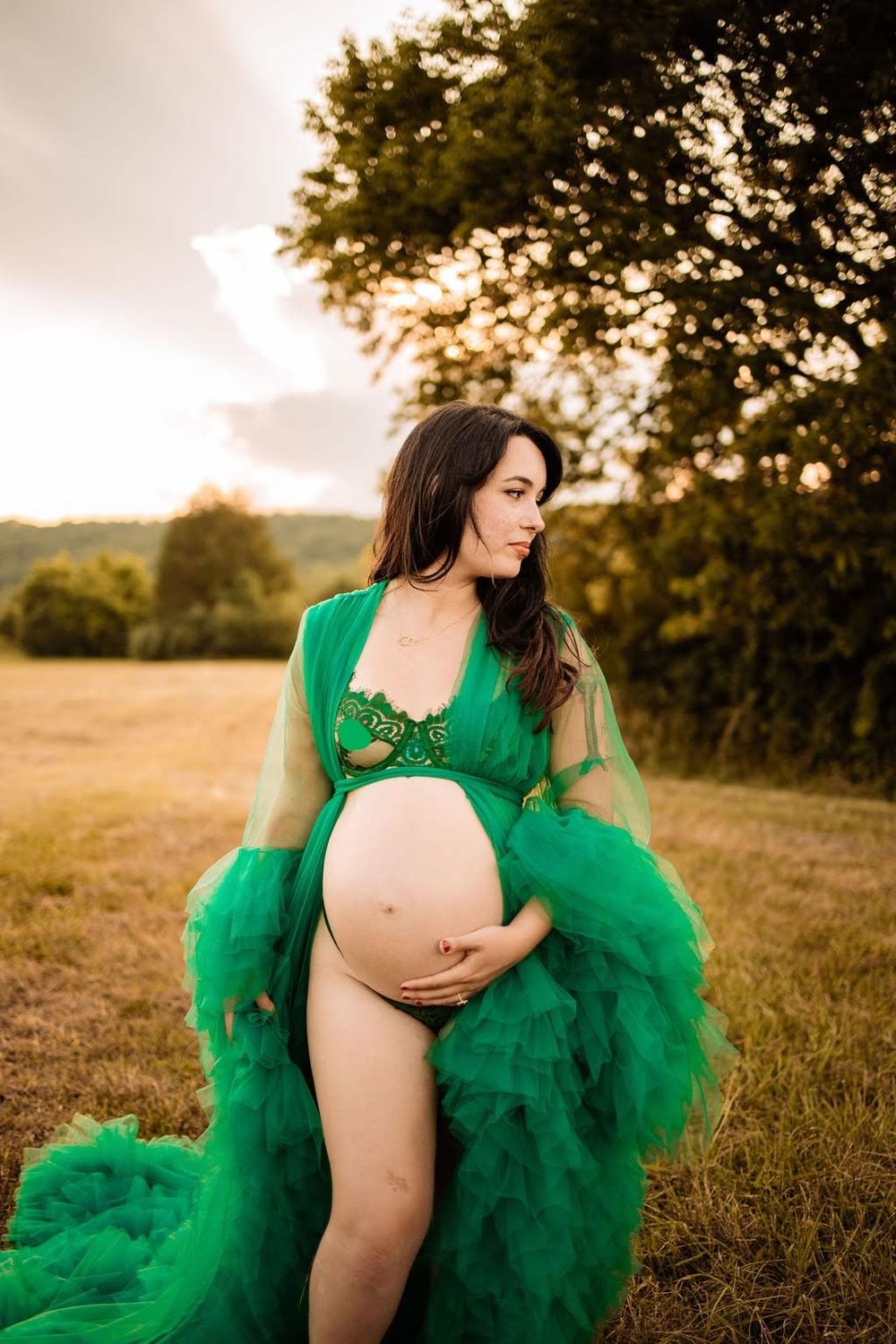 Pregnant woman in green tulle robe holding baby bump in golden hour outdoor field in Oak Ridge, TN.