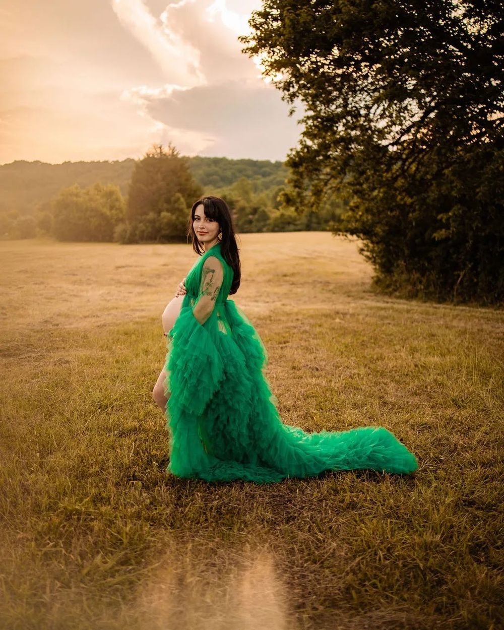 Woman in elegant green tulle gown posing in golden field at sunset with lush trees in background in Oak Ridge, TN.