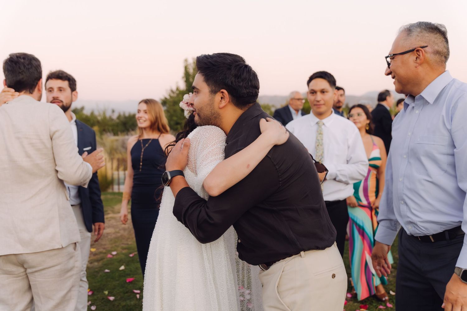 Wedding guests embracing the bride and groom during a warm outdoor reception celebration.