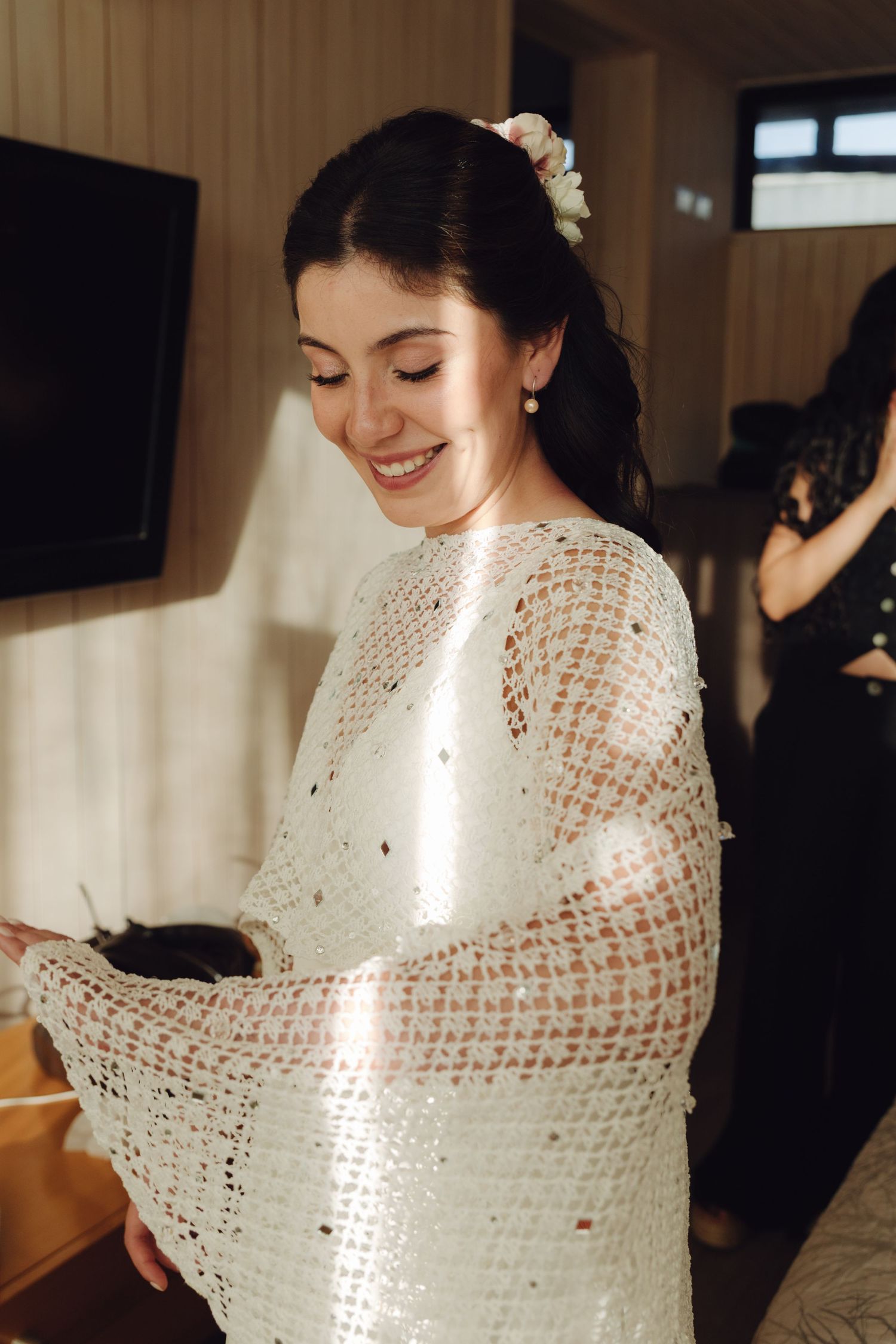 A smiling bride wearing a beautiful white crochet wedding cape in warm sunlight.