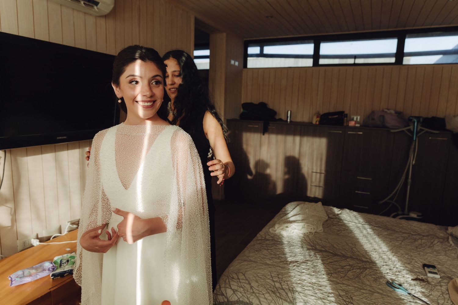 A radiant bride in a white wedding dress smiling in a sunlit room before her wedding.
