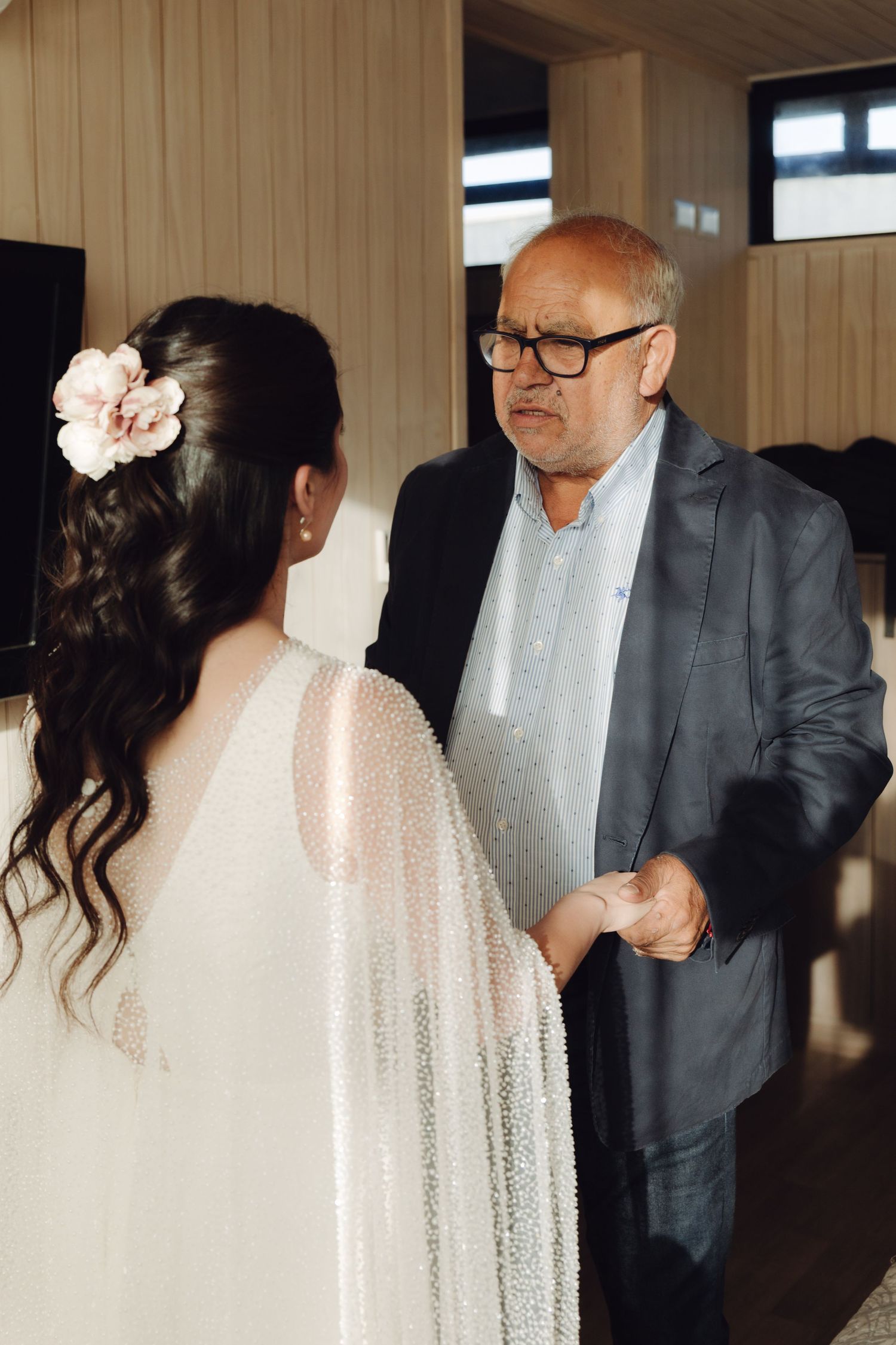 A bride in a white beaded cape holding hands with her father before the wedding ceremony.