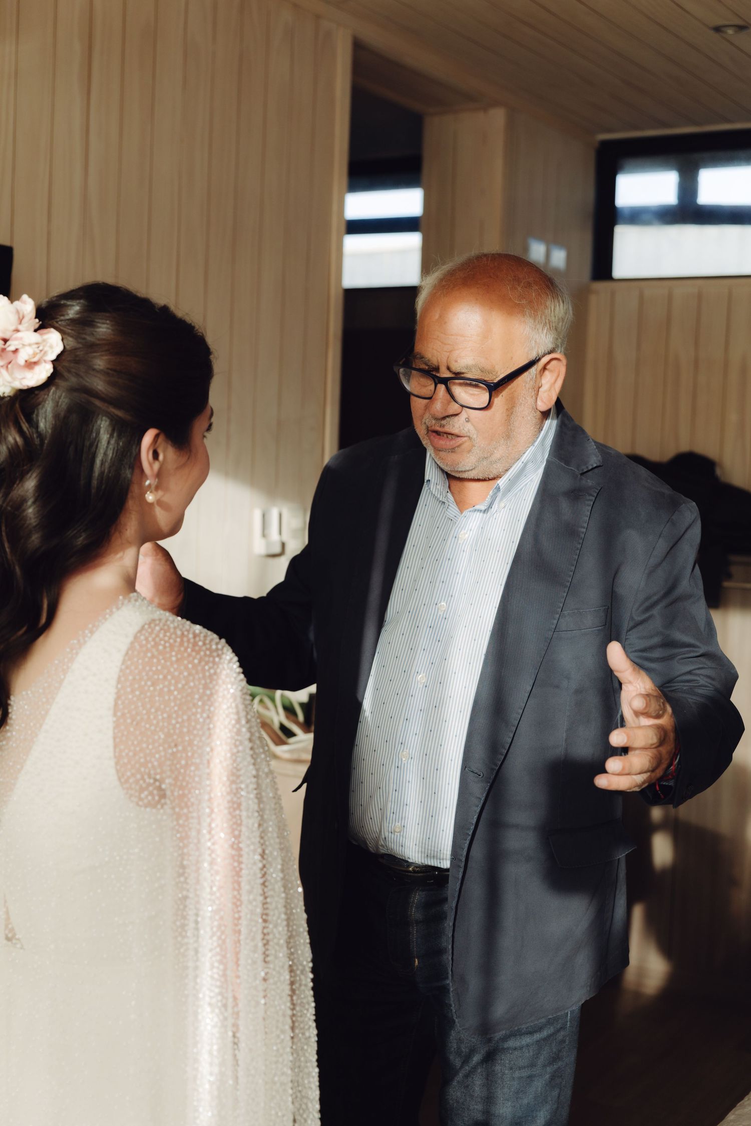 A bride in a white beaded wedding cape having a heartfelt moment with her father.