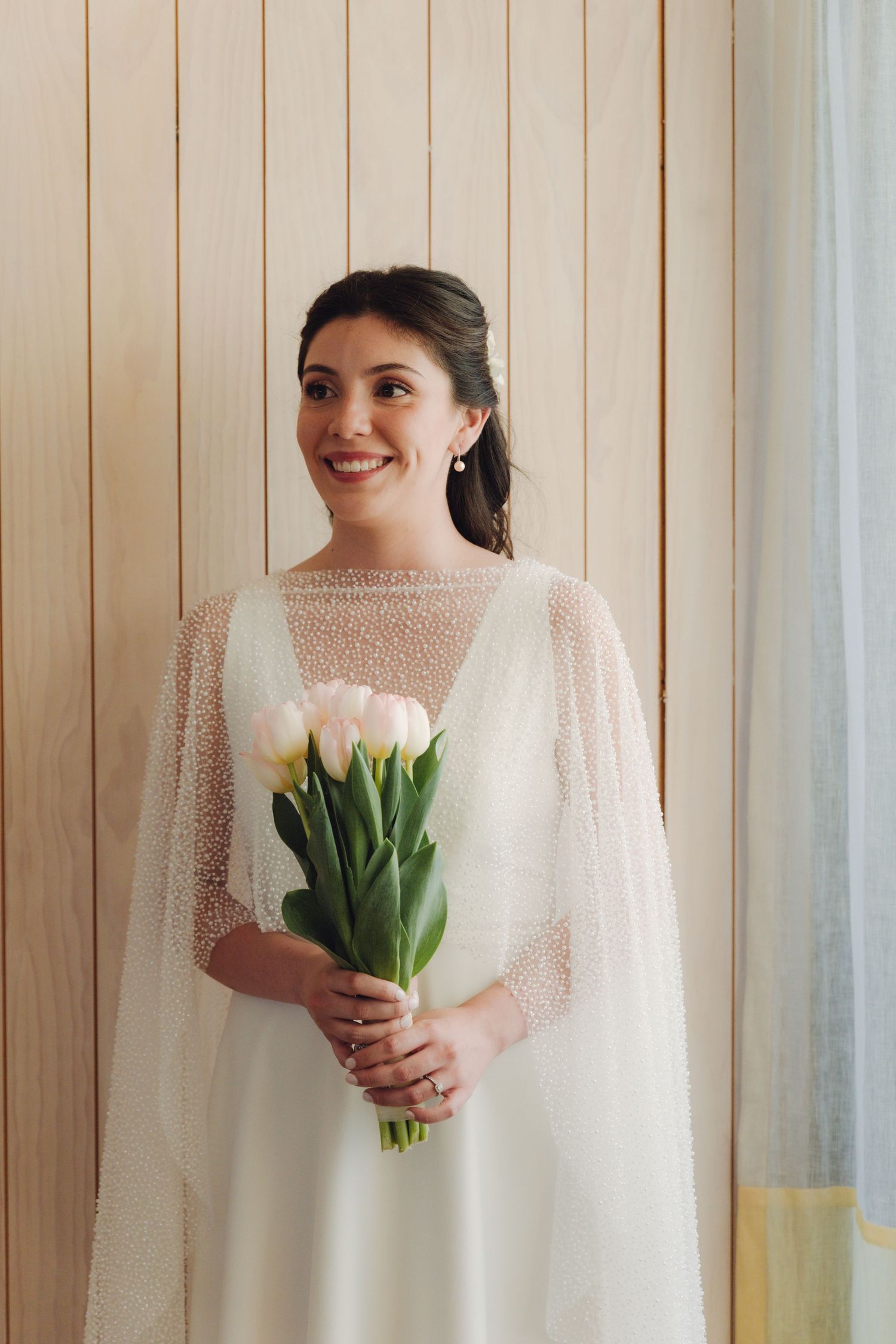 A beautiful bride in a white beaded cape holding white tulips and gazing to the side.