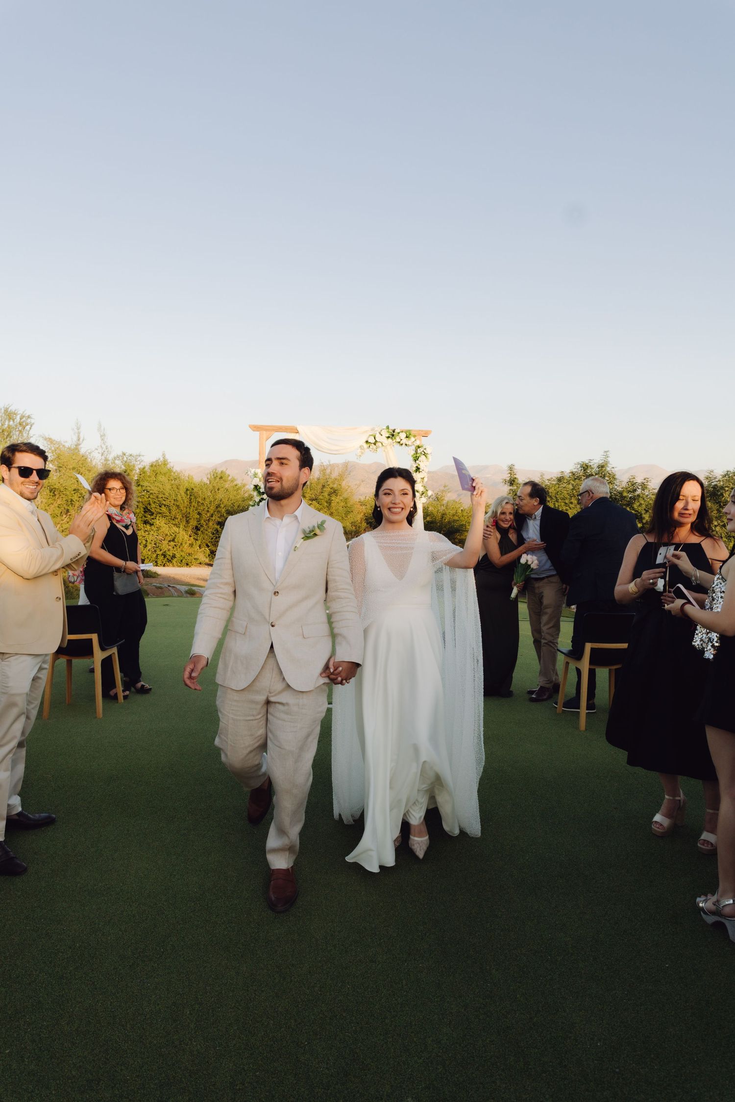 Newlyweds walk hand in hand down the aisle after outdoor wedding ceremony at sunset.