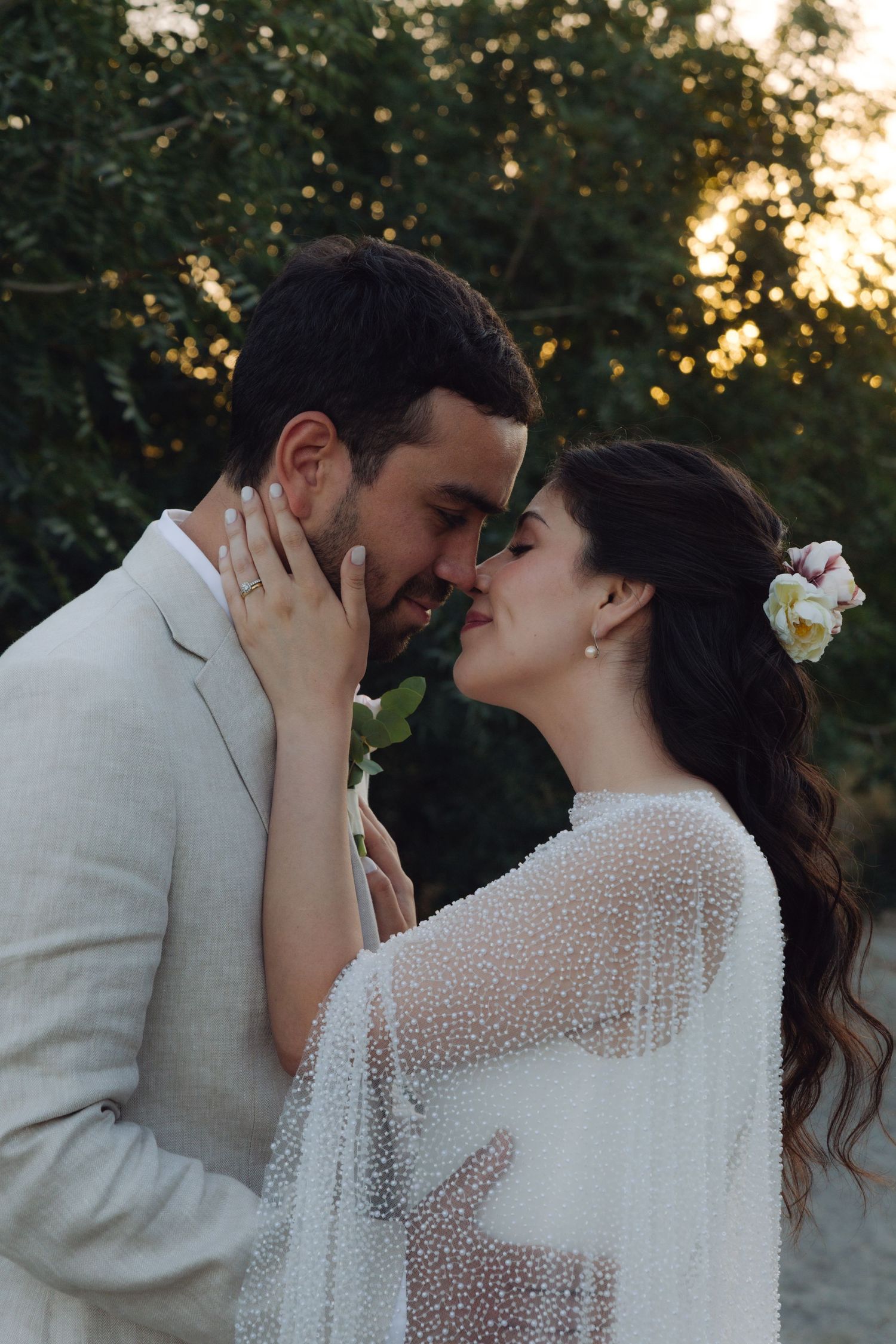 Bride and groom share a tender kiss in a lush garden setting during golden hour.