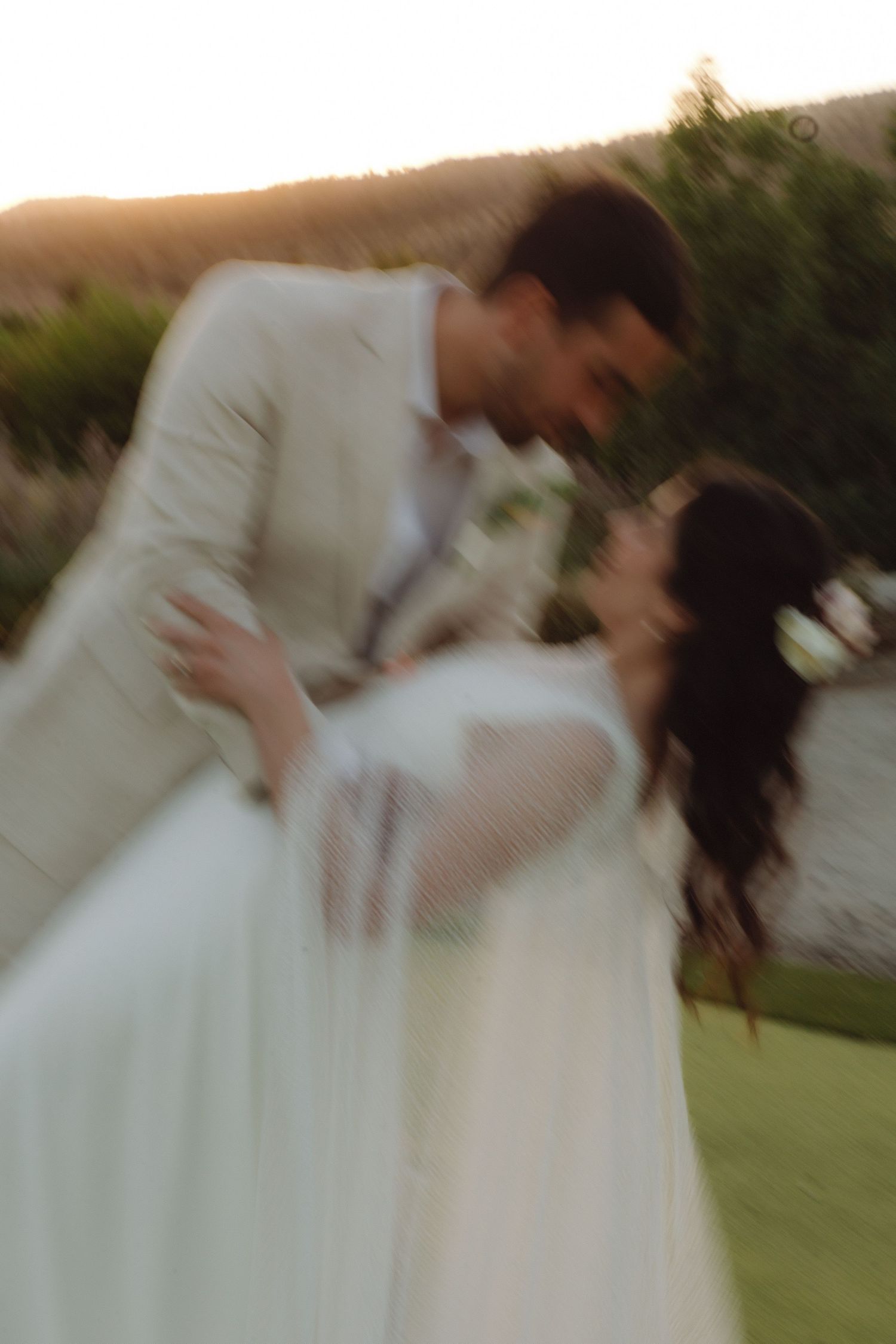 Blurry artistic shot of bride and groom nearly kissing at golden hour outdoor wedding.