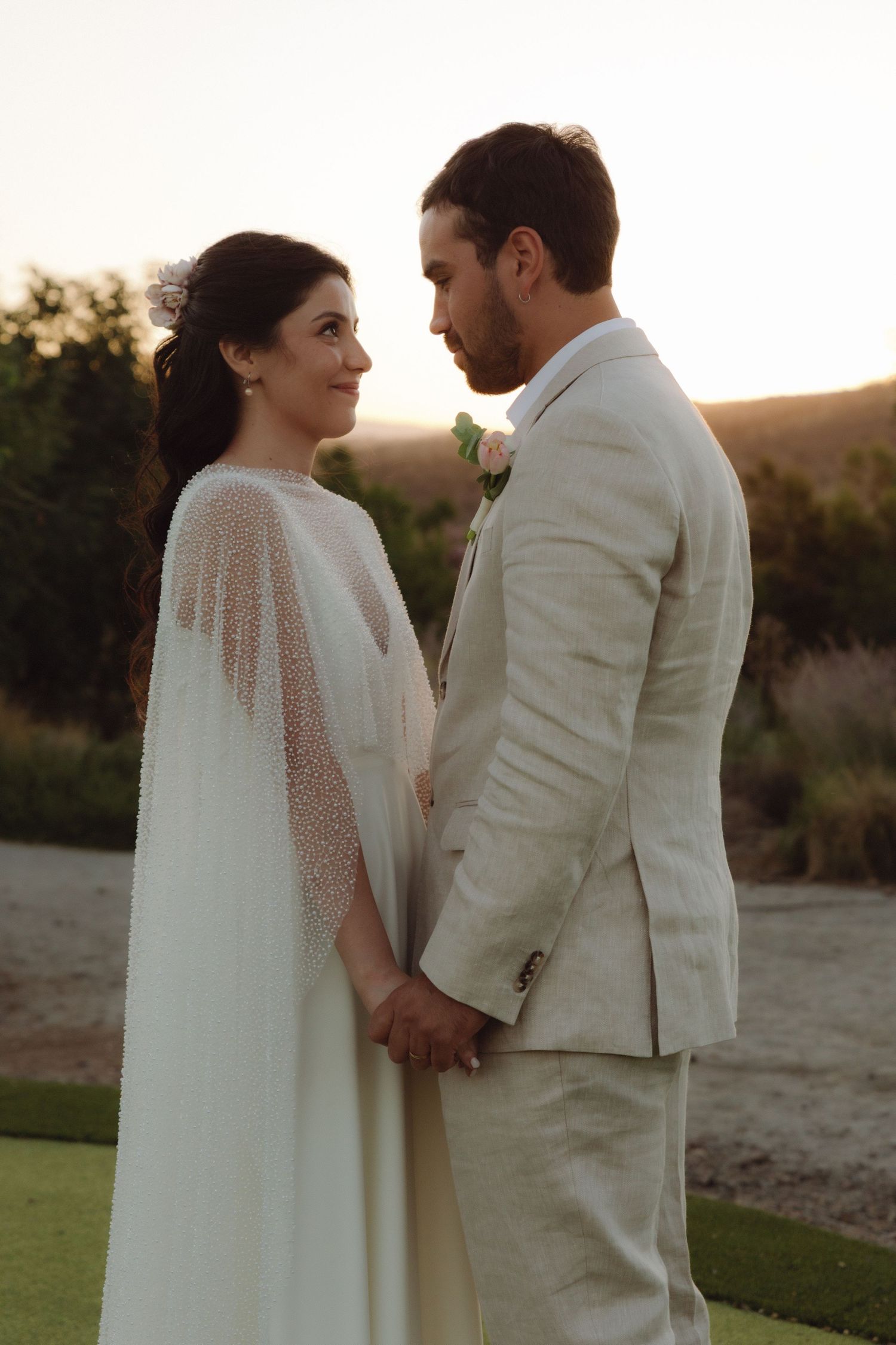 Bride and groom holding hands gazing at each other during sunset wedding portrait.