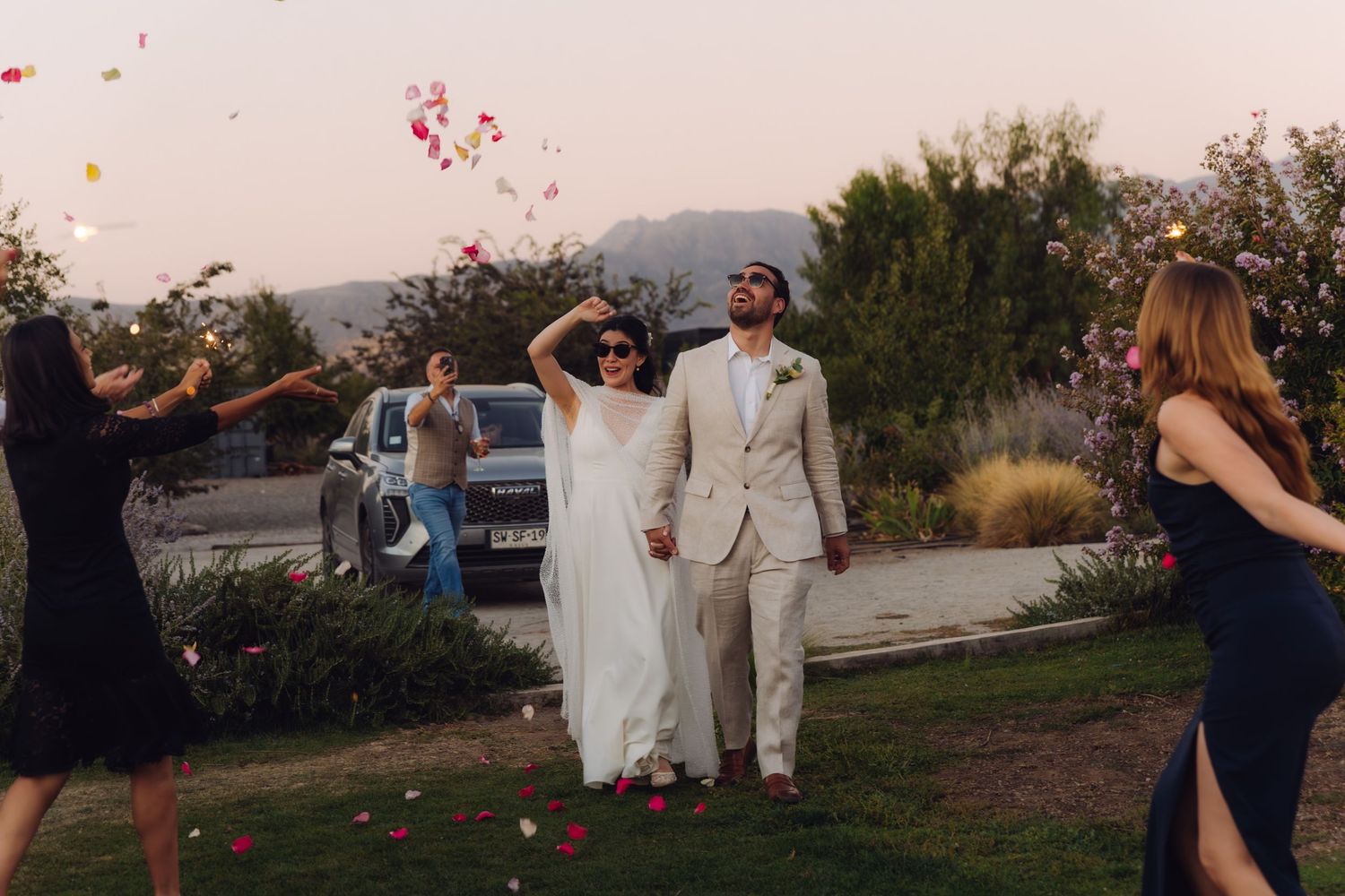 Bride and groom celebrated with colorful rose petal shower by guests at outdoor wedding exit.