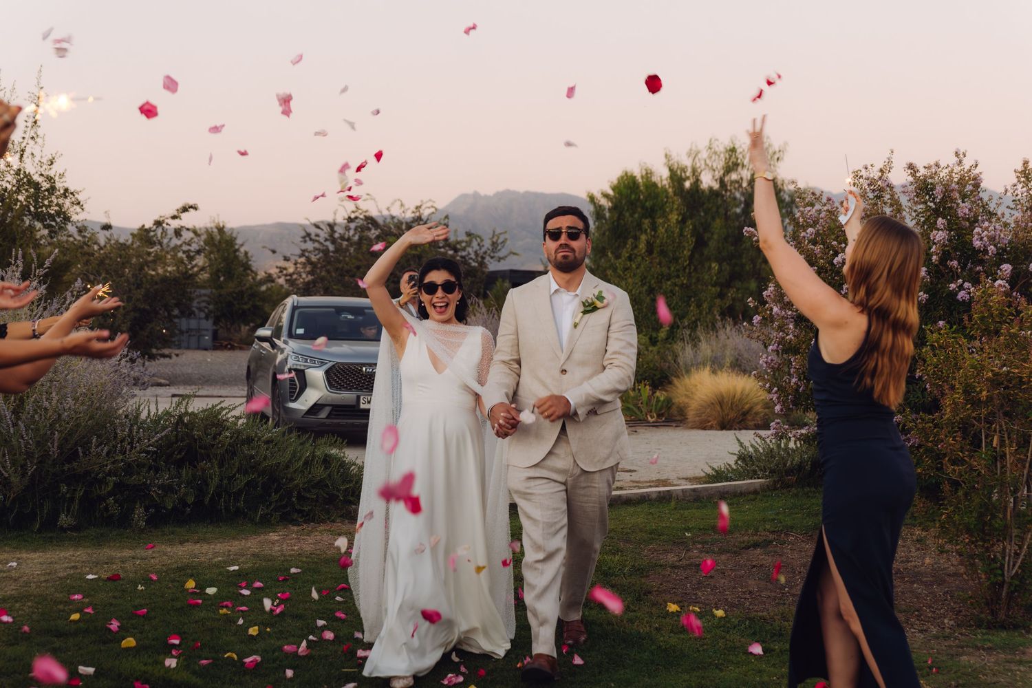 Newlyweds joyfully walking through rose petal shower thrown by guests at outdoor wedding exit.