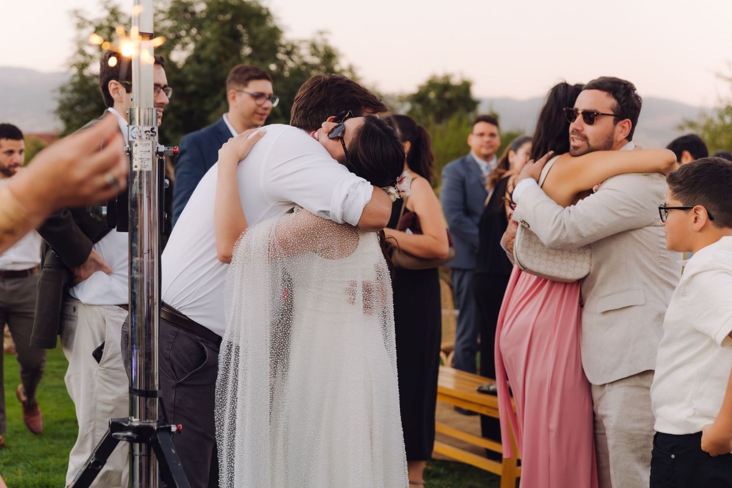 Bride and groom share warm embraces with guests near sparklers at outdoor wedding reception.