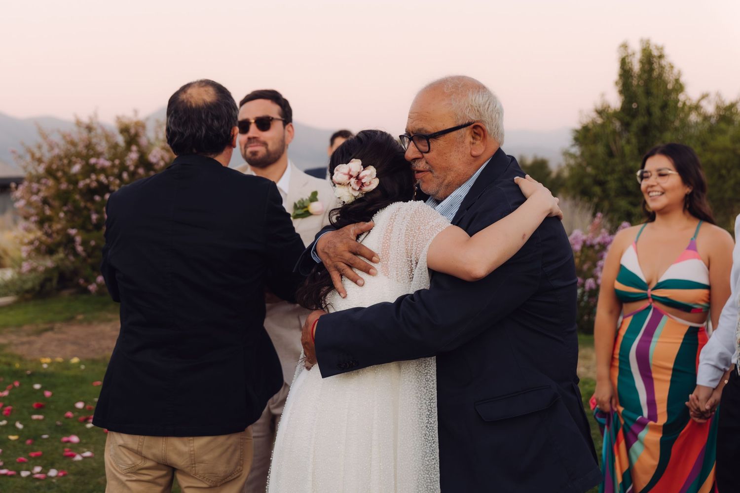 Bride receiving a heartfelt hug from an older gentleman guest at an outdoor wedding reception.