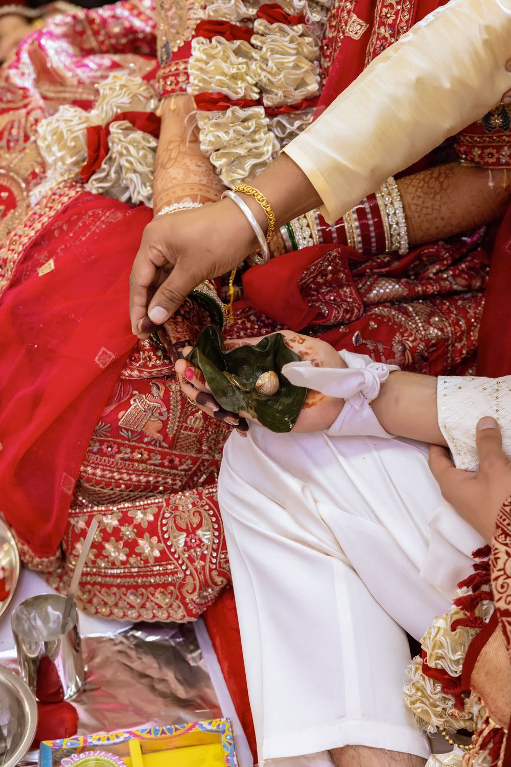 Close-up of Indian wedding ritual with henna-adorned hands holding betel leaves during traditional Hindu ceremony.