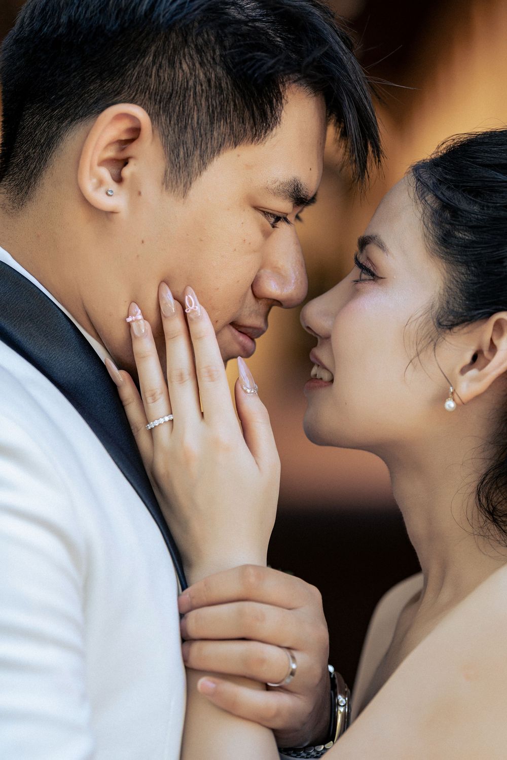 A couple in wedding attire share an intimate moment, foreheads close, wearing matching rings.