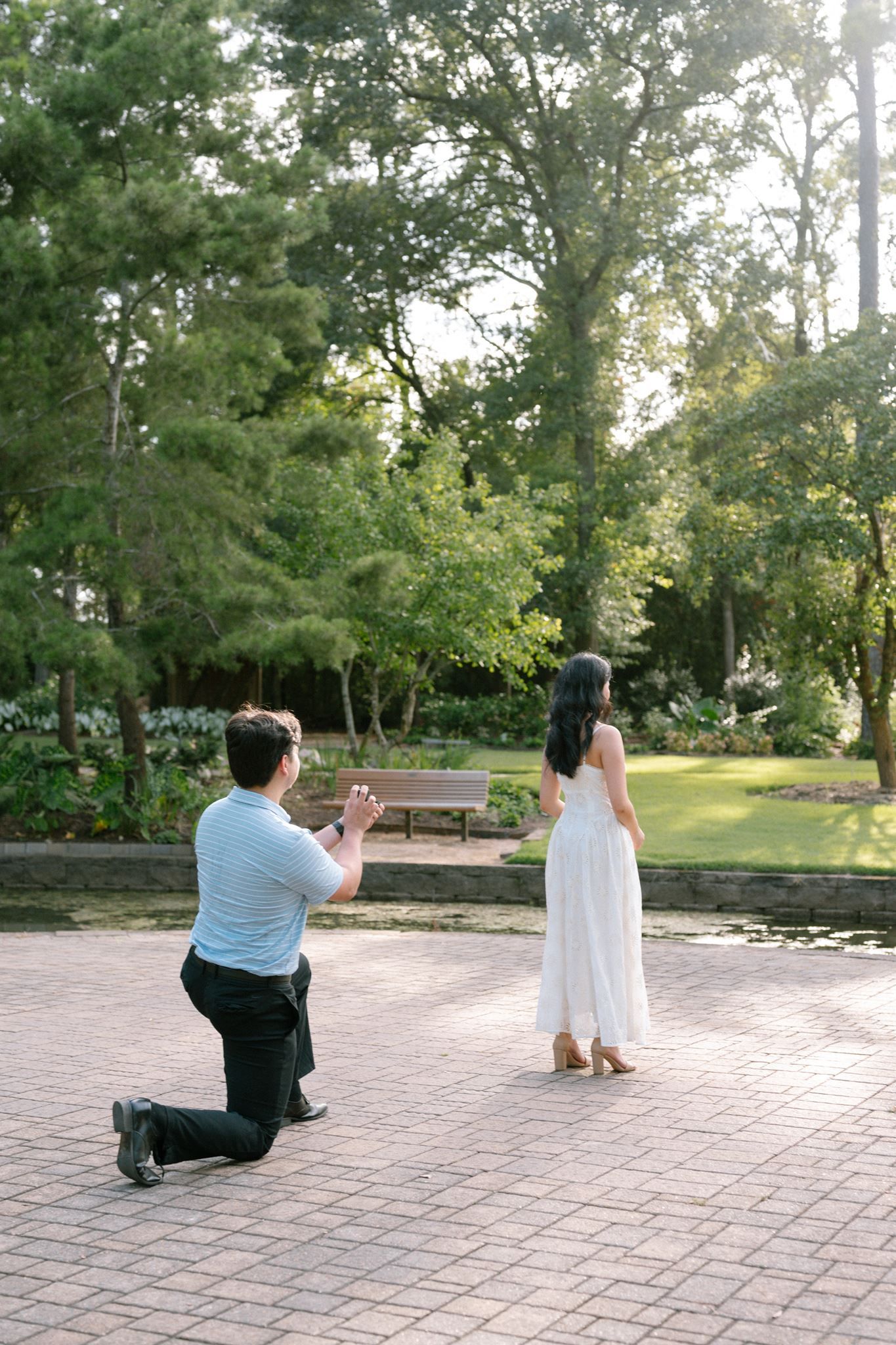 Man kneeling on one knee proposing to woman in white dress at Mercer Botanic garden in Spring, Tx