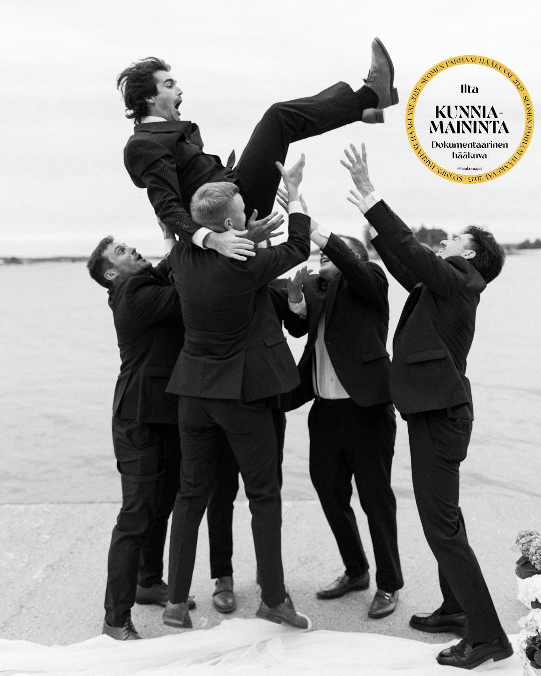 Groomsmen tossing groom in the air in black and white wedding photo with Finnish award seal.