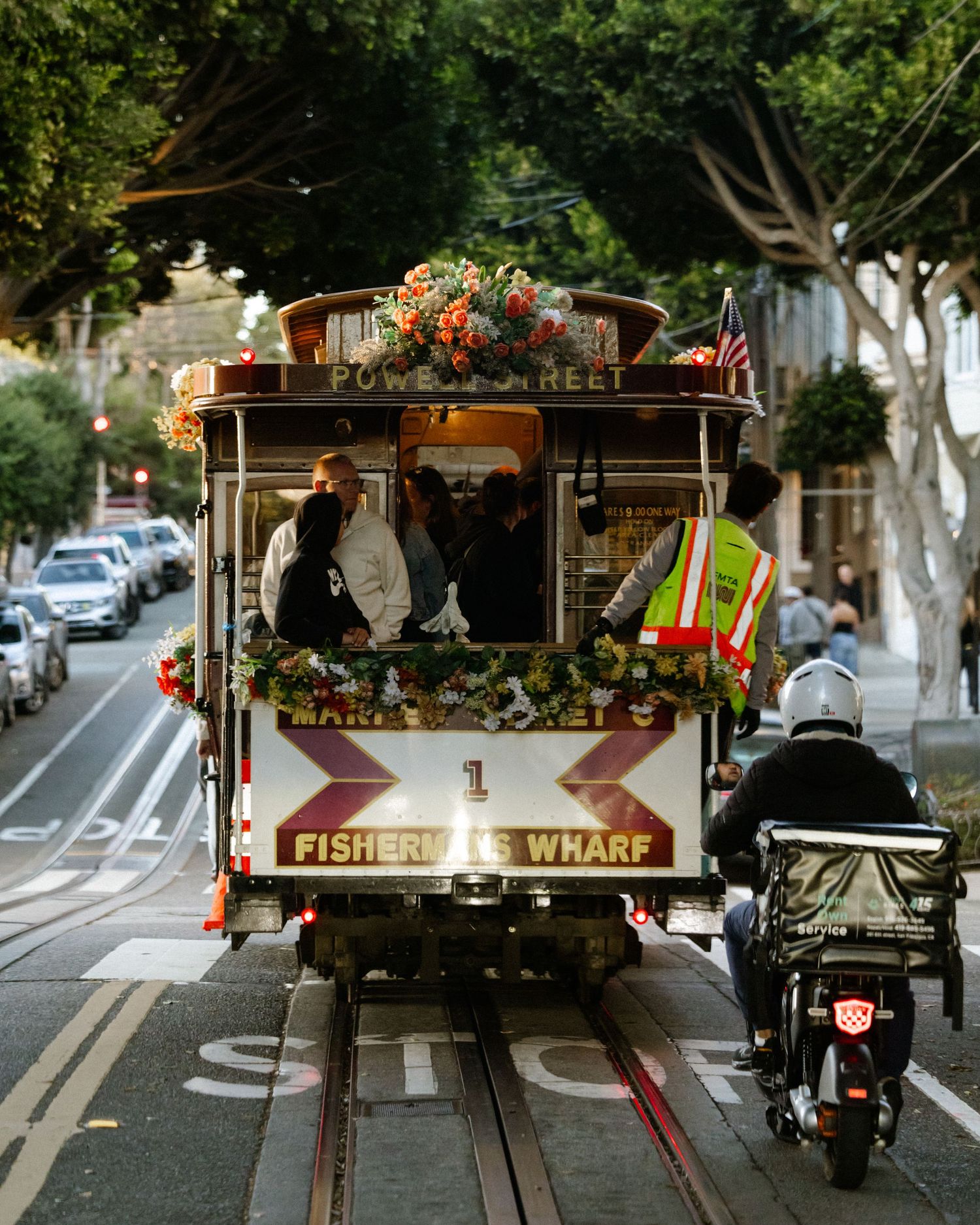 San Francisco cable car No.1 on Powell Street heading to Fisherman's Wharf, decorated with flowers, with a motorcyclist nearby.