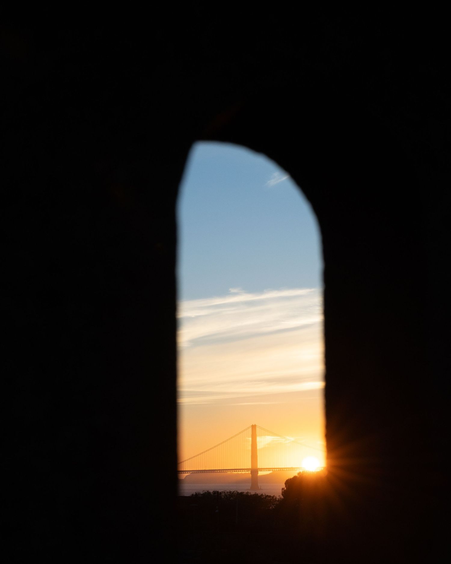 Golden Gate Bridge at sunset viewed through an arched window silhouette in San Francisco.